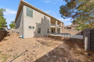 Rear view of property with a fenced backyard, a trampoline, a patio, stucco siding, and a balcony