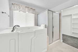 Full bath featuring a spacious closet, a shower stall, light colored carpet, and a garden tub