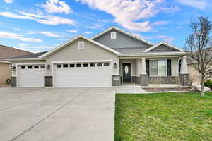 View of front of home with stucco siding, an attached garage, a porch, a front lawn, and brick siding