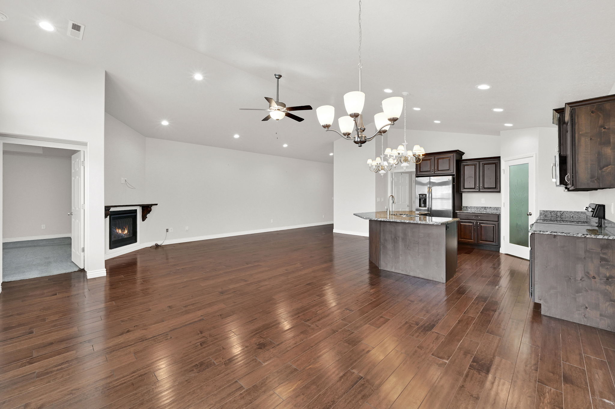 Kitchen with light stone countertops, dark wood finish cabinetry, a glass covered fireplace, ceiling fan, and open floor plan