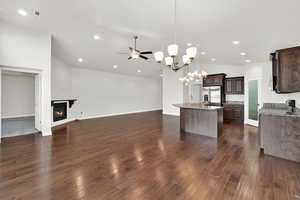 Kitchen with light stone countertops, dark wood finish cabinetry, a glass covered fireplace, ceiling fan, and open floor plan