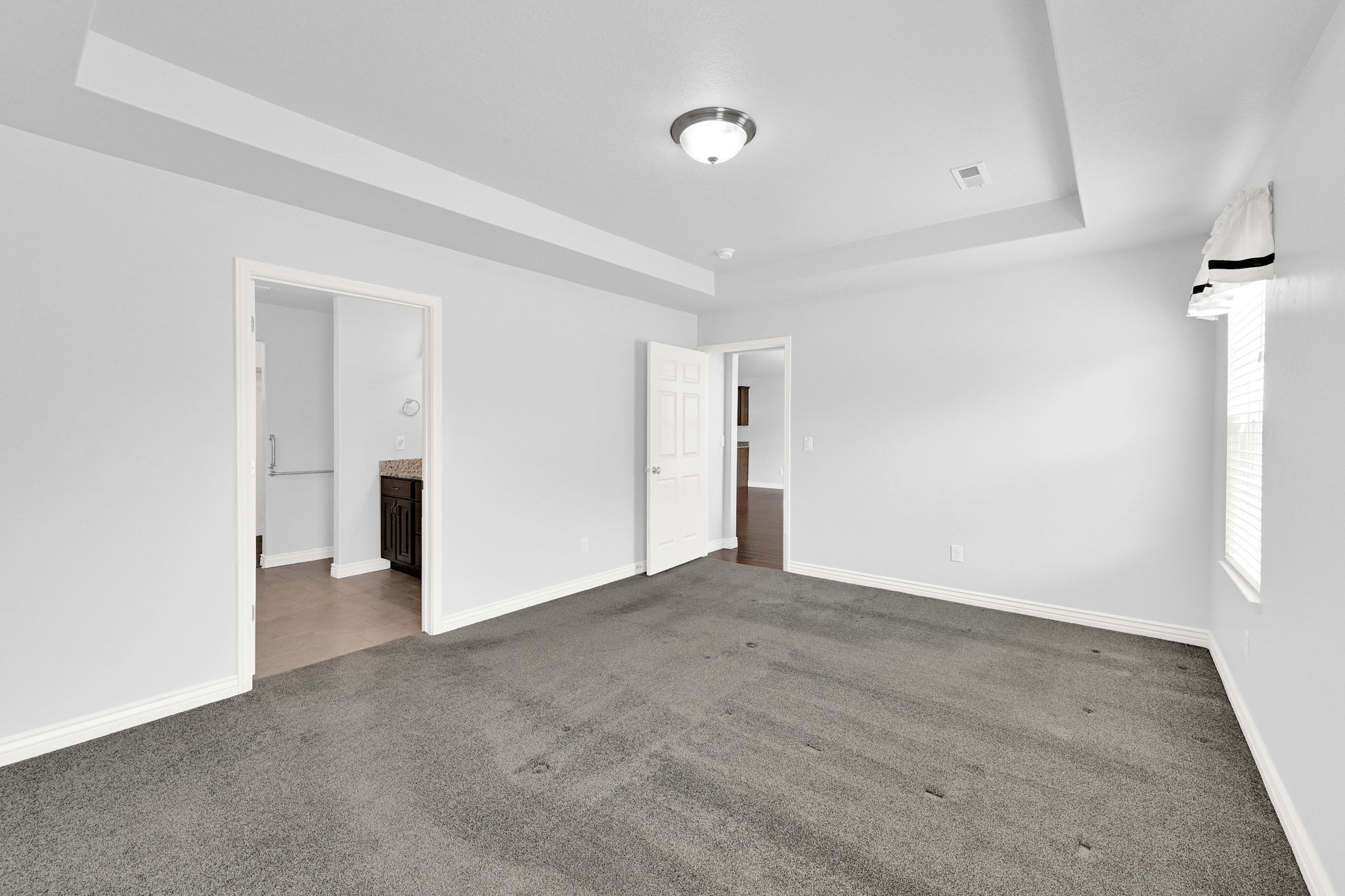 Unfurnished bedroom featuring a tray ceiling, ensuite bathroom, and dark carpet