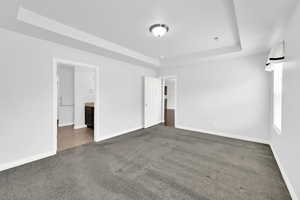 Unfurnished bedroom featuring a tray ceiling, ensuite bathroom, and dark carpet