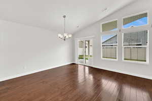 Spare room featuring hanging lights, dark wood finished floors, and lofted ceiling