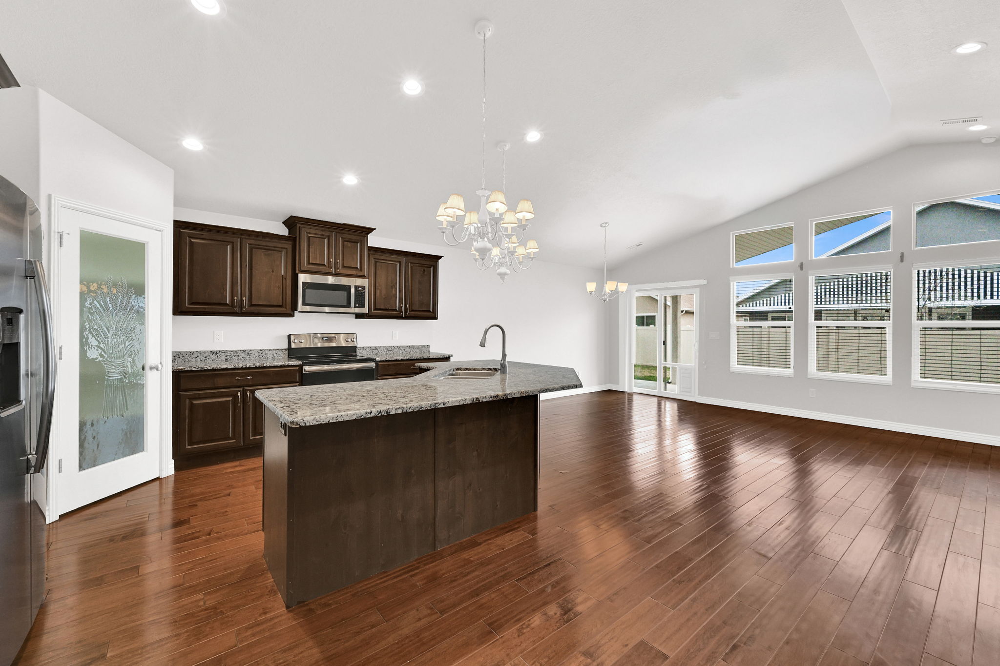 Kitchen featuring hanging lights, dark wood finish cabinets, stainless steel appliances, an island with sink, and light stone counters