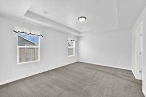 Unfurnished room featuring a tray ceiling and dark carpet