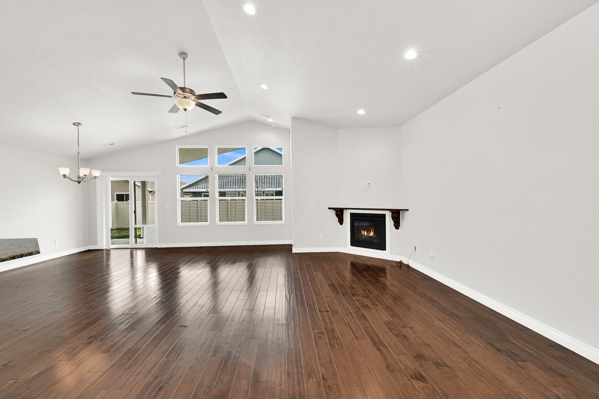 Unfurnished living room with a glass covered fireplace, a ceiling fan, dark wood finished floors, a high ceiling, and a chandelier