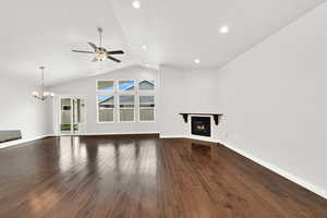 Unfurnished living room with a glass covered fireplace, a ceiling fan, dark wood finished floors, a high ceiling, and a chandelier