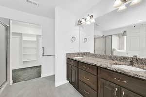 Full bathroom featuring a walk in closet, double vanity, a shower stall, light tile patterned flooring, and light carpet