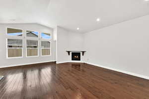 Unfurnished living room with a lit fireplace, dark wood-style floors, vaulted ceiling, and recessed lighting