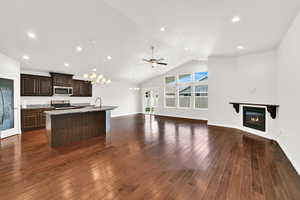 Kitchen featuring dark wood finish cabinetry, open floor plan, a center island with sink, a glass covered fireplace, and hanging lights