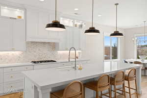 Kitchen featuring glass insert cabinets, light wood-style floors, white cabinetry, and a kitchen bar