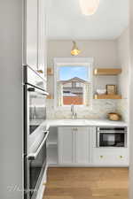 Kitchen featuring stainless steel double oven, white cabinetry, light stone countertops, and light wood finished floors