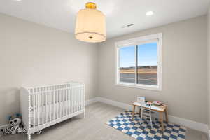 Bedroom with light carpet, a nursery area, and recessed lighting