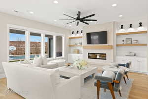 Living area with light wood-style floors, ceiling fan, a brick fireplace, recessed lighting, and built in shelves