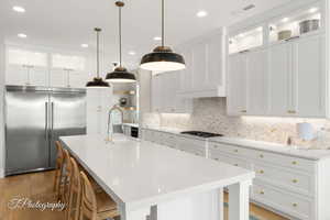 Kitchen featuring glass insert cabinets, a breakfast bar, stainless steel appliances, white cabinets, and an island with sink