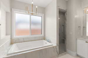 Full bath with a marble finish shower, vanity, a garden tub, and a chandelier