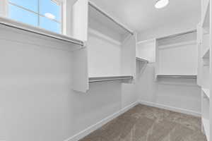 Walk-in closet featuring white built-in shelving, multiple hanging rods, and a window with natural light