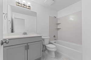 Bathroom featuring a gray vanity with a single sink, an integrated bathtub and shower combination, a toilet, and a large wall-mounted mirror