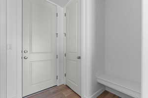 Entry area featuring a solid white door with brushed nickel hardware, wood-finish flooring, and a built-in bench