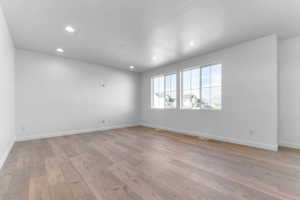Spacious room featuring light wood-finish flooring, recessed lighting, and a white color palette