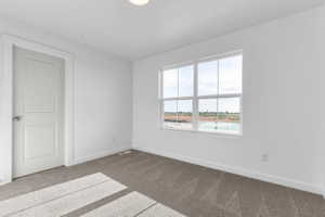Bright interior room featuring a multi-pane window, neutral carpet, white baseboards, and a white panel door with polished hardware