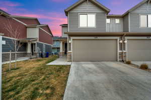 View of front of home with stone siding, driveway, an attached garage, and a lawn