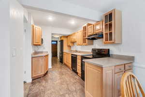 Kitchen with glass fronted cabinets, black appliances, light countertops, light wood finish cabinets, and recessed lighting