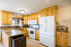 Kitchen with white appliances, light wood finished floors, a peninsula, open shelves, and dark stone counters