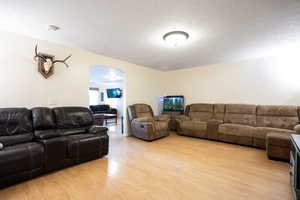 Living area with arched walkways, light wood-style flooring, and a textured ceiling
