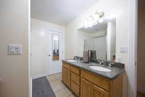 Full bathroom featuring double vanity, light tile patterned floors, and a stall shower