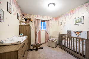 Bedroom featuring light colored carpet, a nursery area, and a textured ceiling