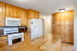 Kitchen featuring white appliances, arched walkways, light wood-style flooring, and light stone countertops