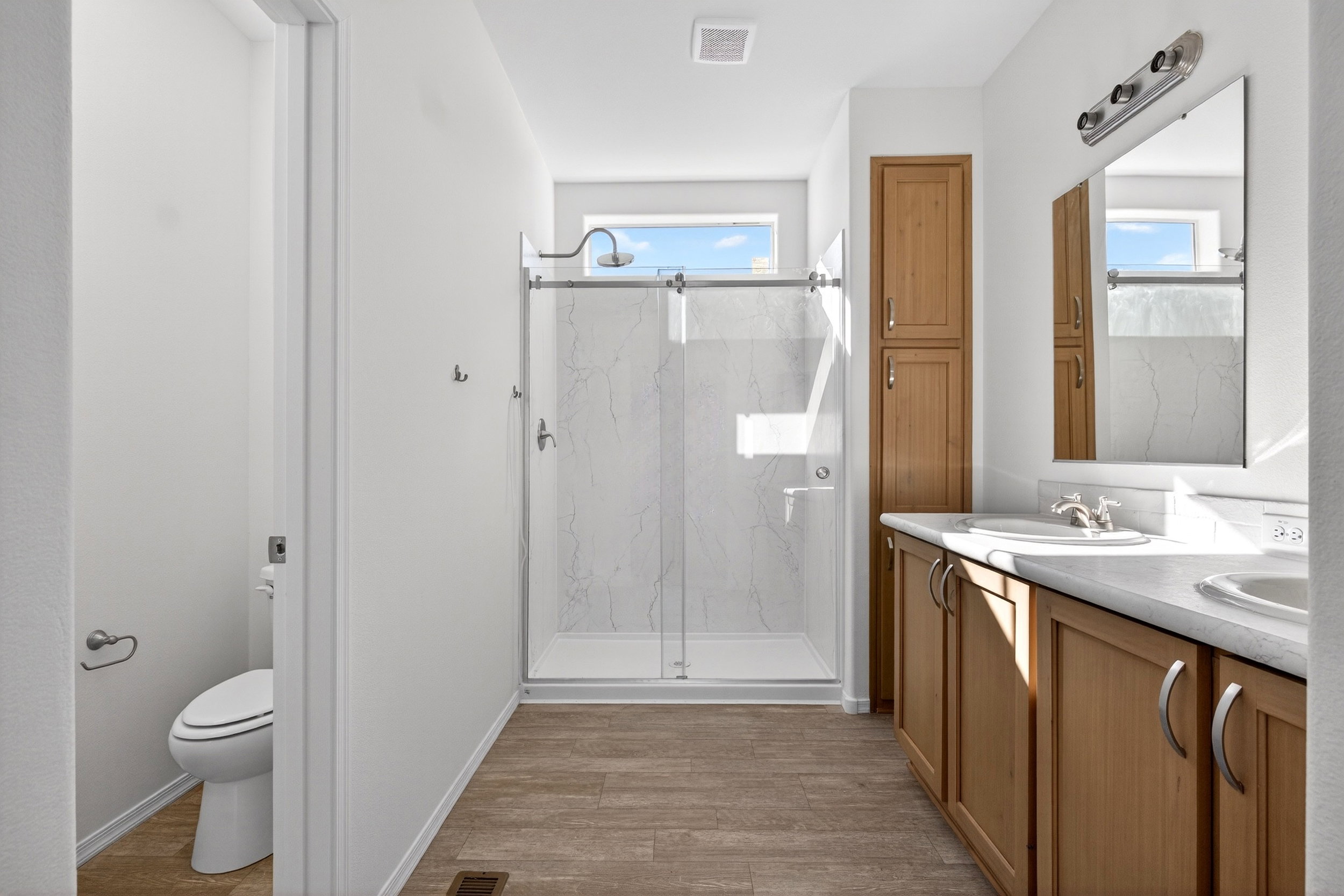 Full bathroom featuring double vanity, a marble finish shower, and light wood-style flooring