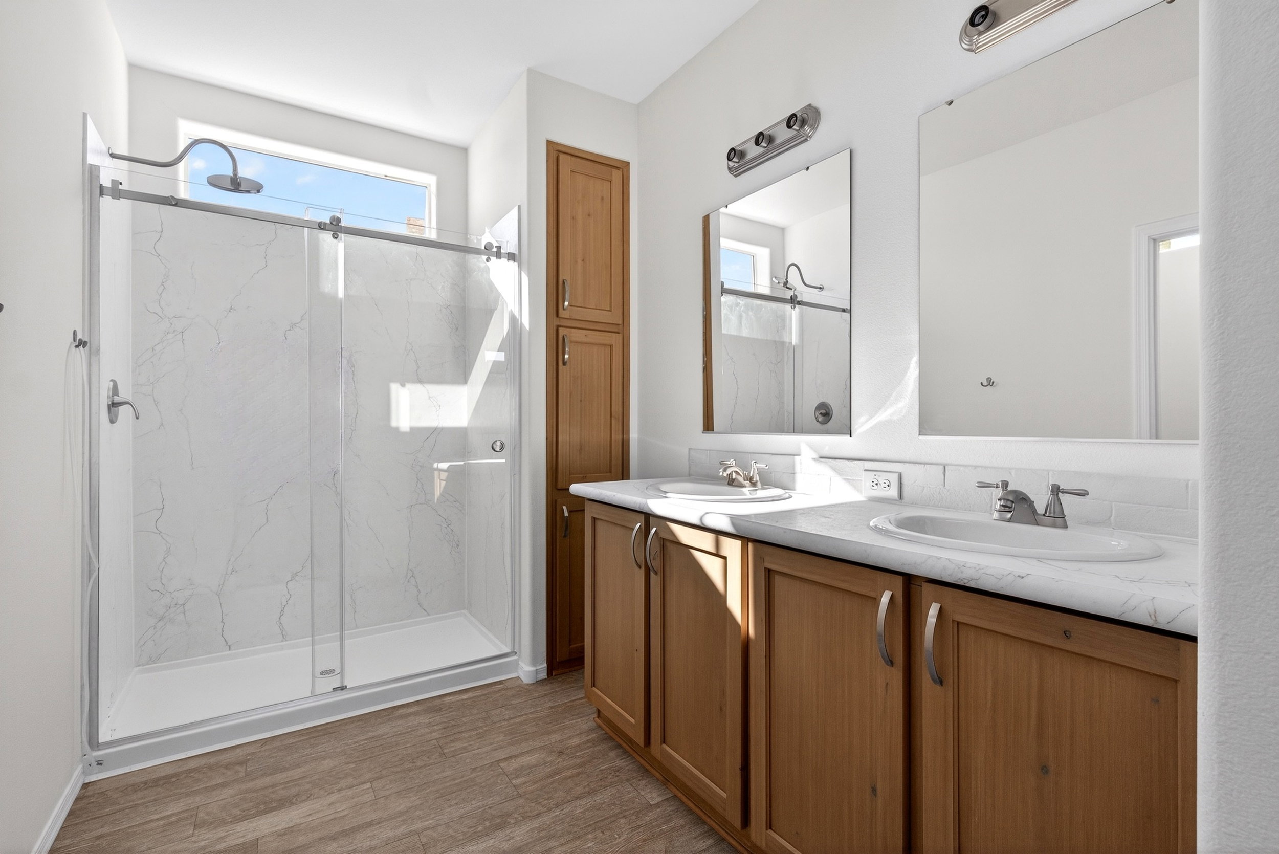 Bathroom featuring double vanity, a marble finish shower, and dark wood-style floors