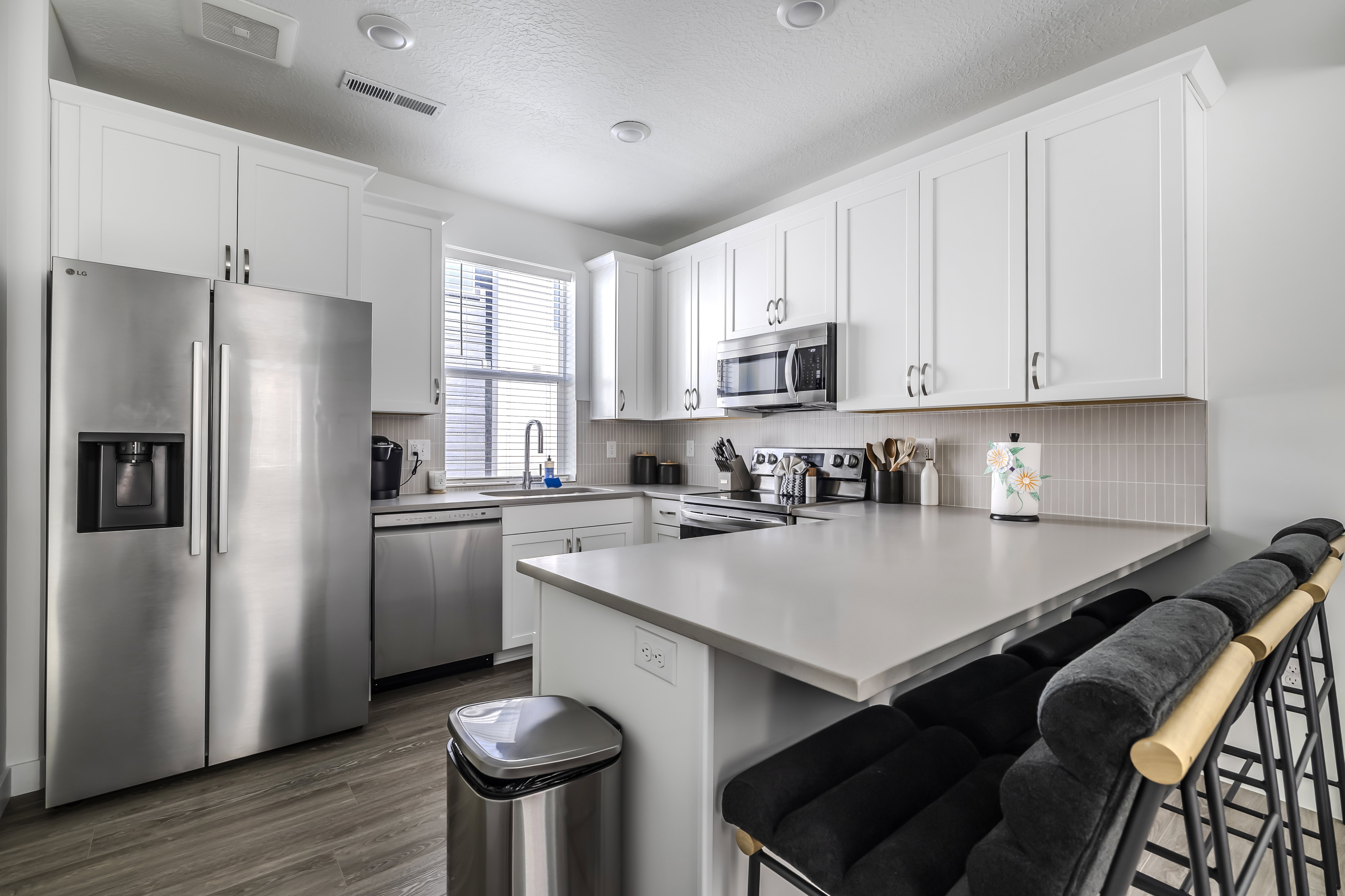 Kitchen with stainless steel appliances, a peninsula, a breakfast bar, white cabinets, and light countertops
