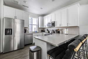 Kitchen with stainless steel appliances, a peninsula, a breakfast bar, white cabinets, and light countertops