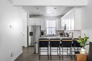 Kitchen with a peninsula, a breakfast bar area, stainless steel appliances, white cabinetry, and dark wood-style flooring