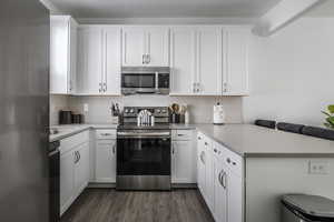 Kitchen featuring stainless steel appliances, a peninsula, white cabinetry, a breakfast bar area, and light countertops