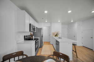 Kitchen featuring white cabinets, stainless steel appliances, a breakfast bar area, light wood-style floors, and light stone countertops
