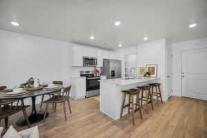 Kitchen featuring a breakfast bar, stainless steel appliances, white cabinetry, a peninsula, and light wood-style floors