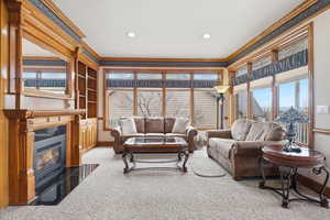 Living area with crown molding, light carpet, built in features, and a fireplace with flush hearth