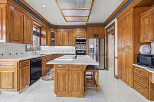 Kitchen with ornamental molding, black appliances, a breakfast bar area, light countertops, and a center island