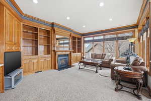 Living room with crown molding, built in features, light colored carpet, recessed lighting, and a fireplace with flush hearth