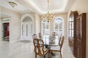 Dining area with hanging lights, light tile patterned flooring, ornamental molding, and a tray ceiling