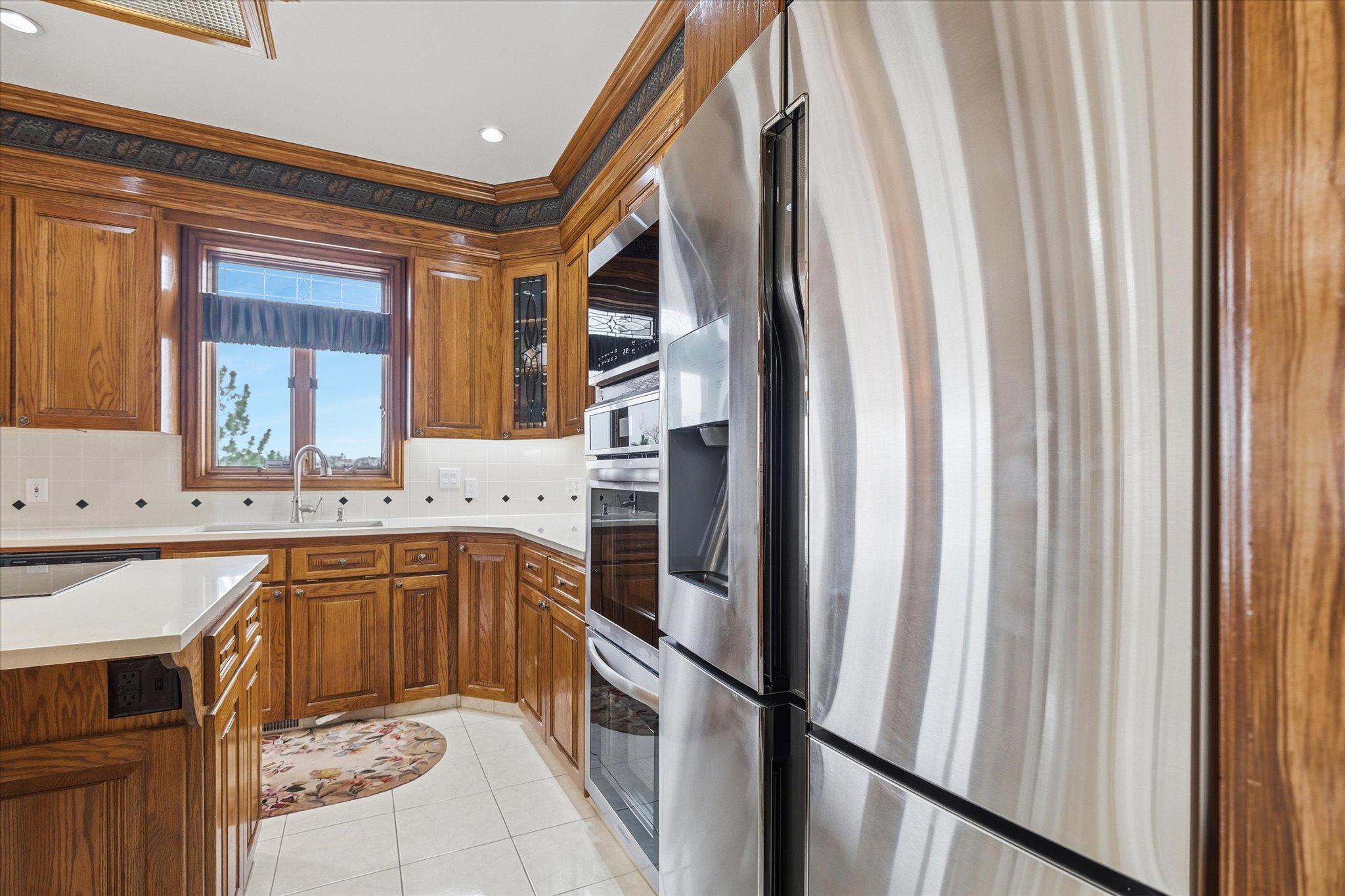 Kitchen featuring light countertops, stainless steel appliances, light tile patterned floors, wood finish cabinets, and ornamental molding