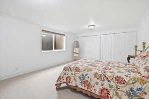 Bedroom with ornamental molding, multiple closets, and light carpet