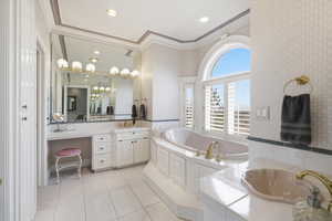 Bathroom with wallpapered walls, two vanities, crown molding, a garden tub, and light tile patterned floors