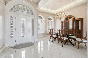 Foyer entrance with hanging lights, crown molding, a raised ceiling, and light tile patterned flooring