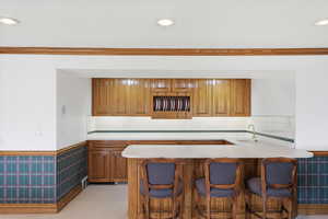 Kitchen with wood finish cabinetry, a breakfast bar, a wainscoted wall, a peninsula, and ornamental molding